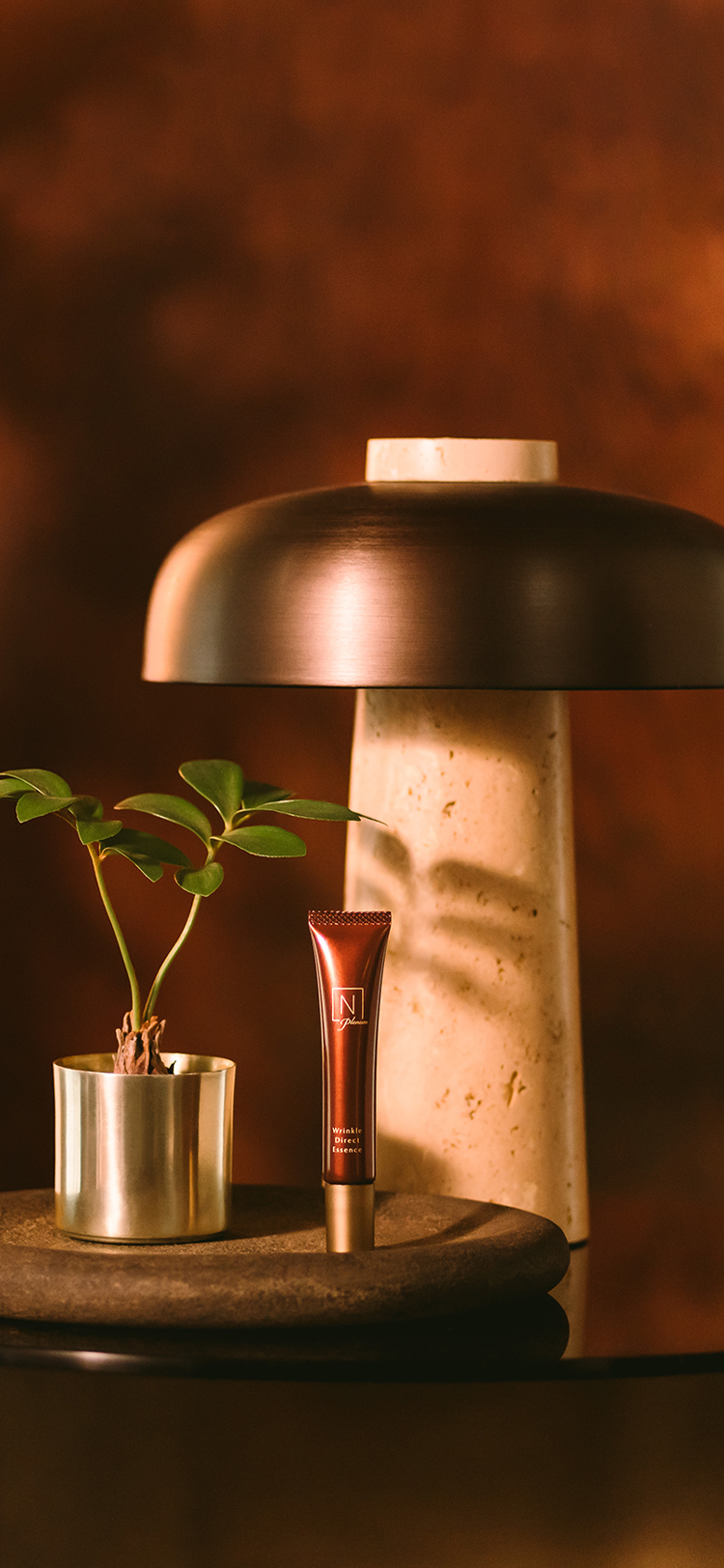 臙脂色の背景にN organic Plenumの「リンクルダイレクト　エッセンス」の商品がオシャレなアイテムの置いてあるテーブルに展示されている写真 