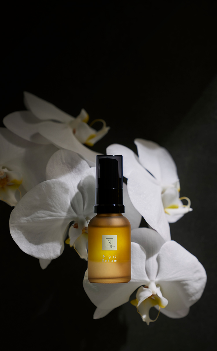 N organic Vie モイストリペアナイトセラムの瓶が胡蝶蘭の前に暗い中で浮いて写っている写真